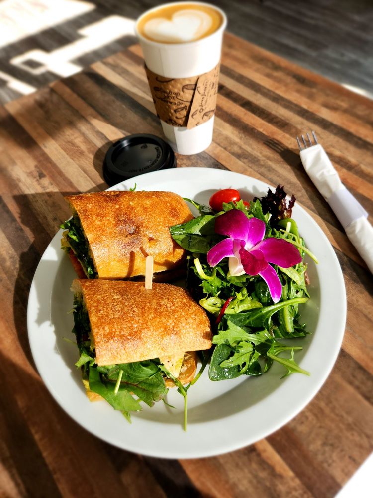 Sandwich with a side of greens and a latte on a sunlit table at the cafe